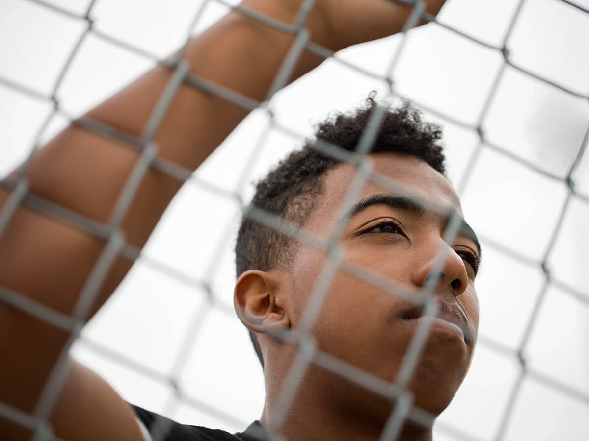 Teenage Black boy holding a chain-link fence.