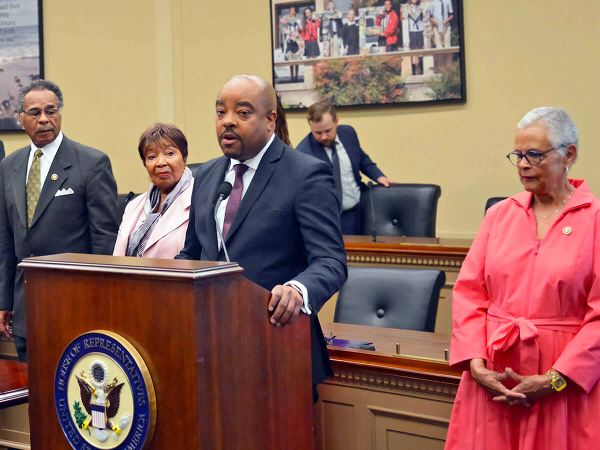 Dr. Michael Lindsey speaking at a podium, surrounded by Congresswoman Bonnie Watson Coleman and other elected officials and taskforce experts