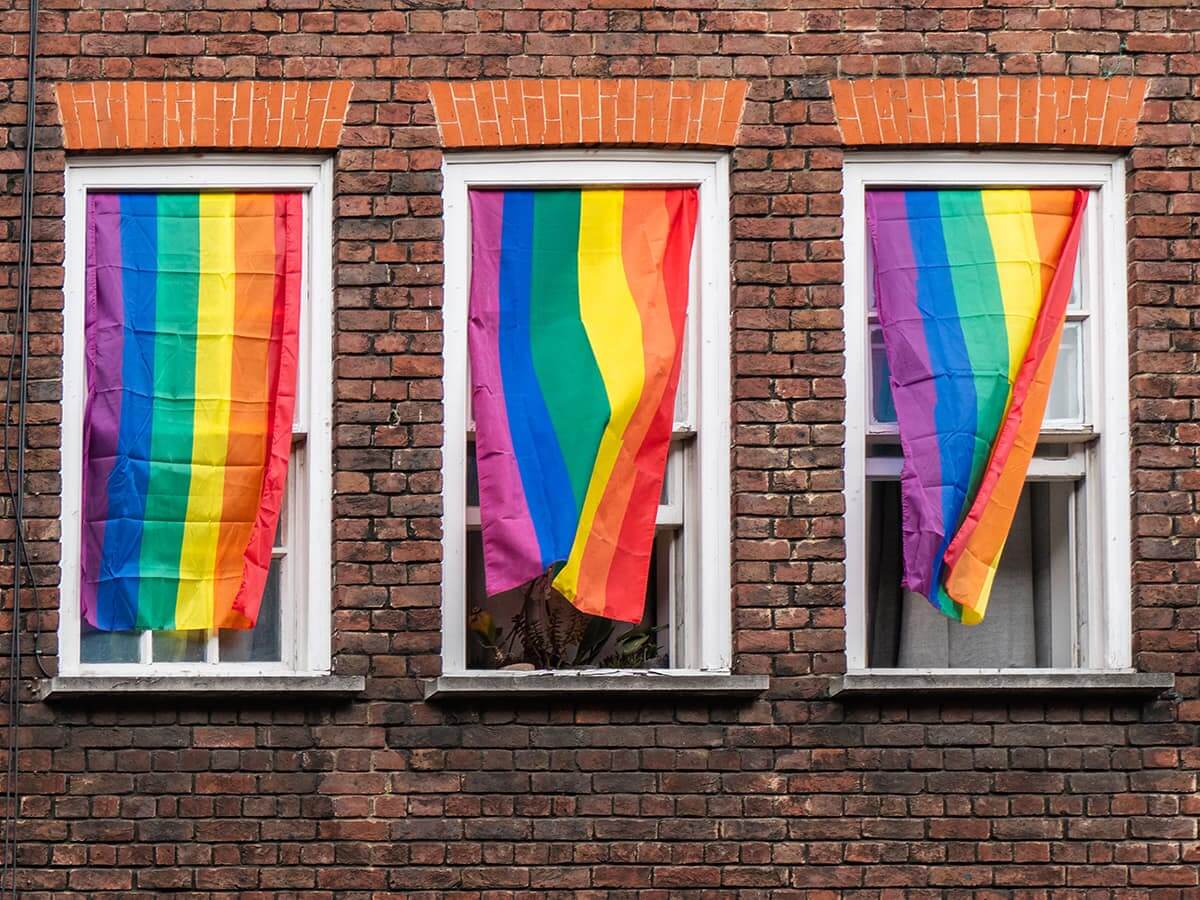 Photo of apartment windows with rainbow flags hanging as curtains