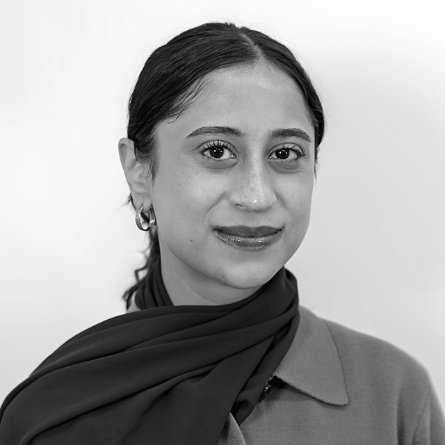 Black and white photo of Aamir smiling at the camera wearing a scarf