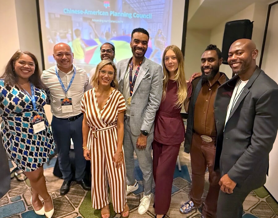 A diverse group of panelists standing in a line, posing for a photo in a hotel conference room